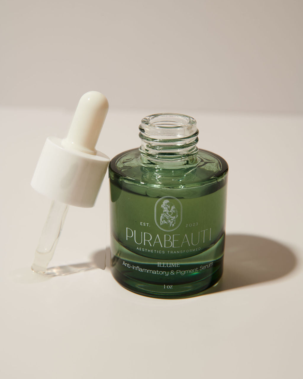 A clear glass bottle with a dropper containing a greenish liquid, labeled Purabeauti Illume Serum anti-inflammatory, anti-bacterial , and anti-fungal