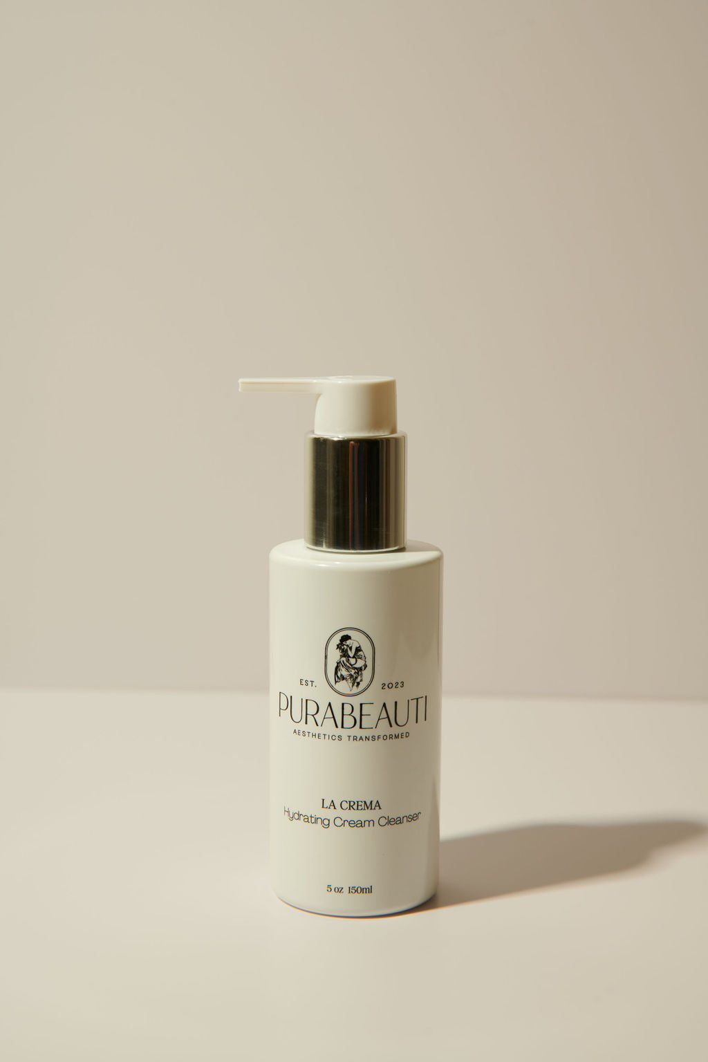 A pump bottle of Purabeauti La Crema cleanser against a neutral background.